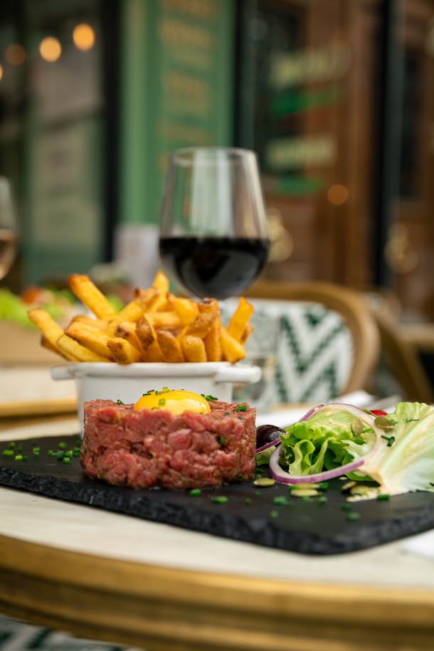 Assiette de tartare de bœuf avec salade, frites maison et verre de vin.